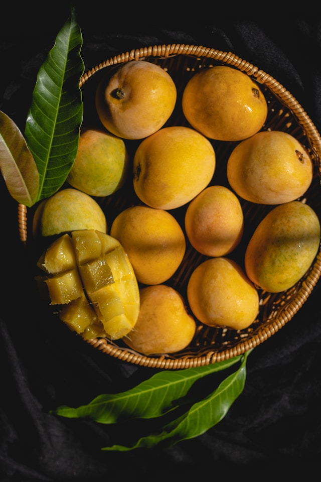a photo of 10 ripe alphonso mangoes in a wicker basket.